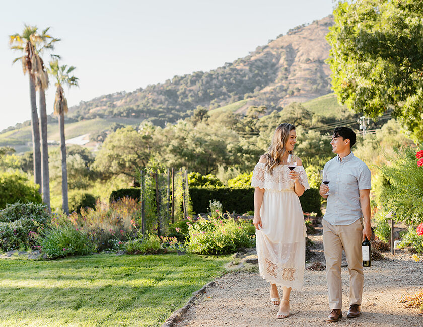 A woman and man walking through the gardens at Stags' Leap with a glass of wine in hand. 